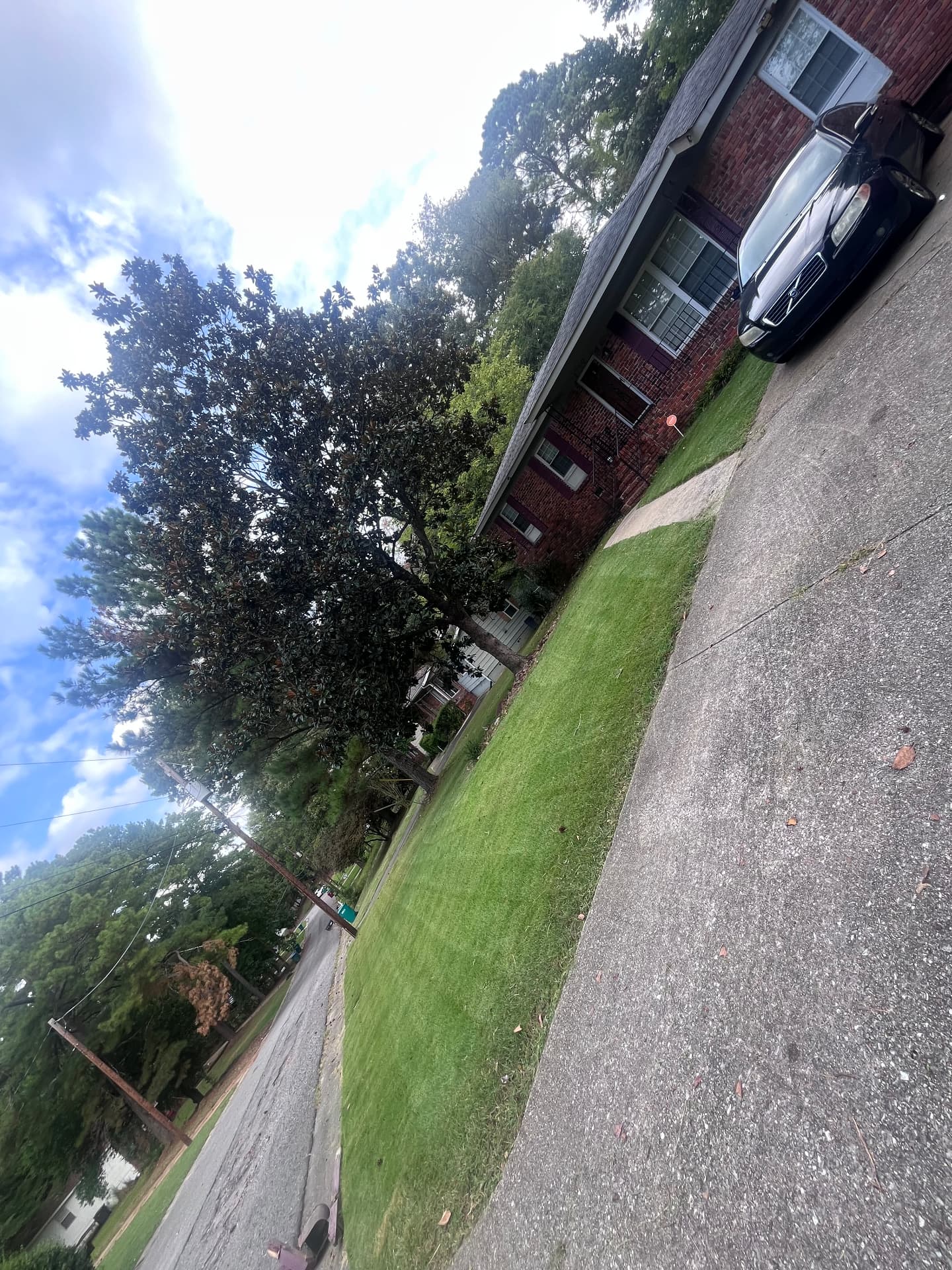 Red brick house with a concrete driveway, a parked car, and a narrow strip of short green grass.