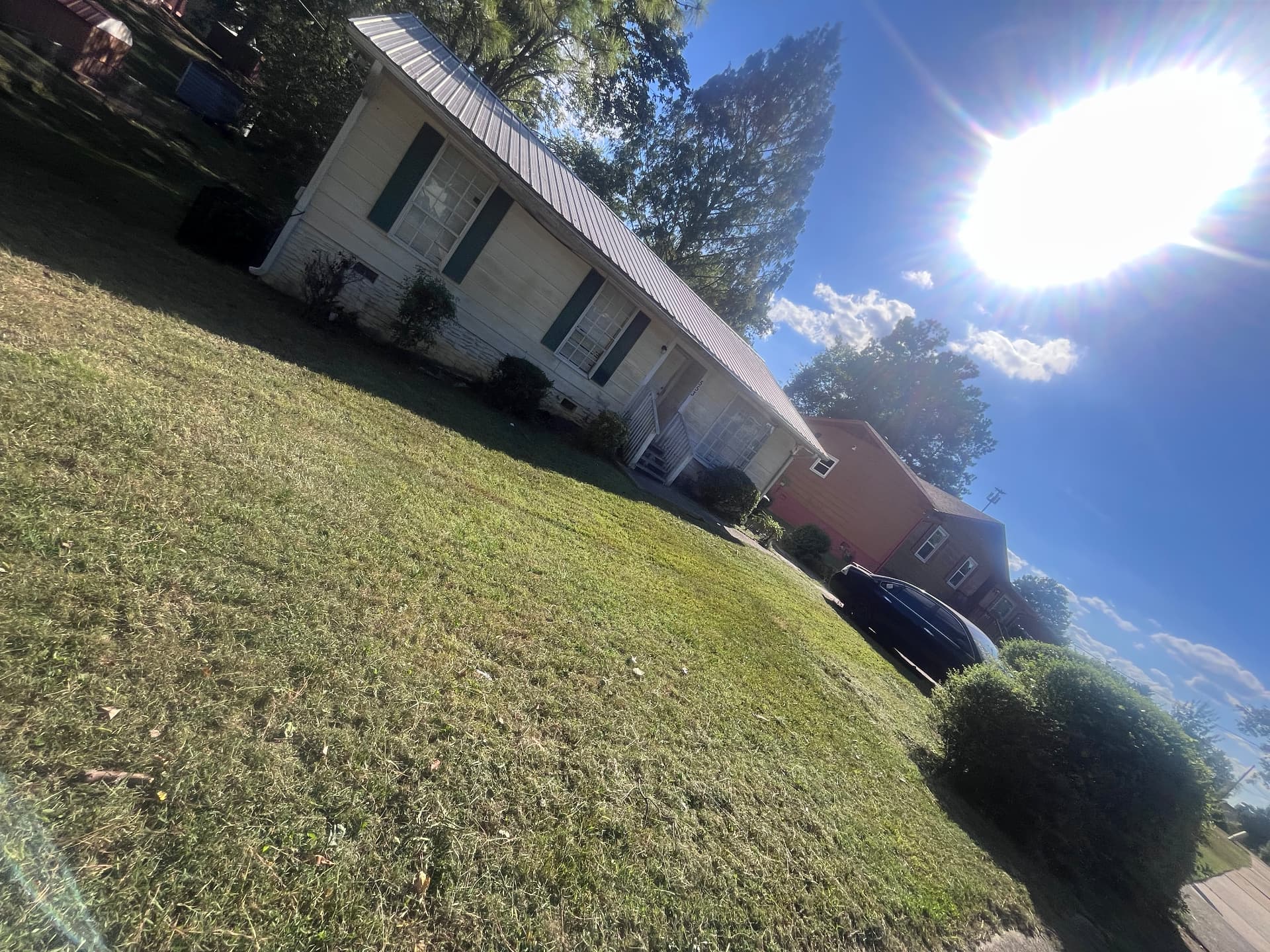 Freshly mowed front lawn in front of a cream-colored house with green shutters and a white porch.